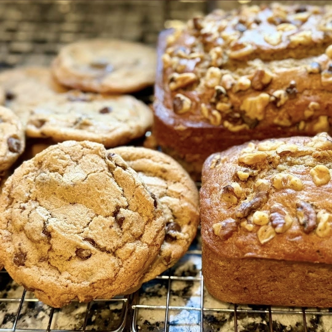 Fresh chocolate chip cookies and walnut-topped sourdough loaves cooling on a rack